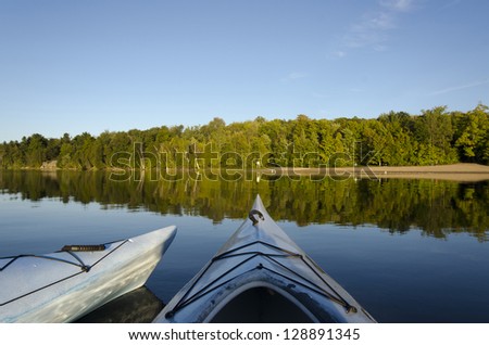 Two kayaks floating on calm Charleston Lake facing the beach with the evening light