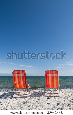 Lounging beach chairs on the Lake Ontario shoreline with large copy space area in the deep blue sky