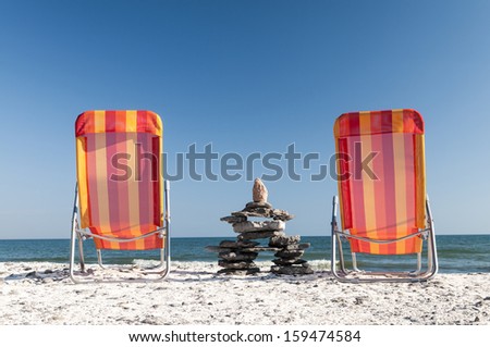 To chairs at the beach facing onto Lake Ontario with a stone formation between the chairs