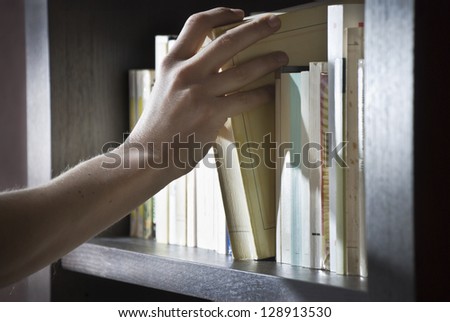 Close shot of a right hand of a young man picking a book in a bookshelf.