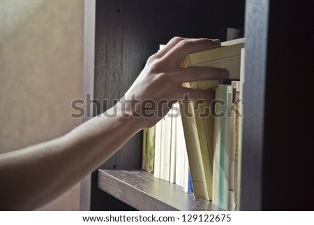 Right hand of a young man picking a book in a bookshelf