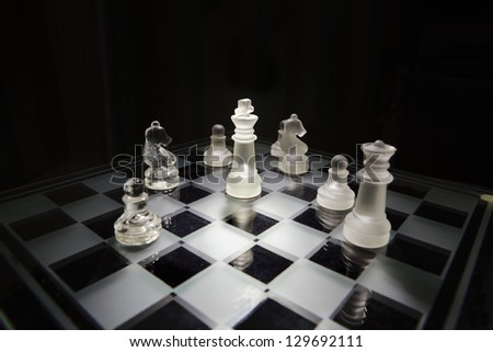 Glass chess game on a black background.The king is in the center and surrounded with different pieces.