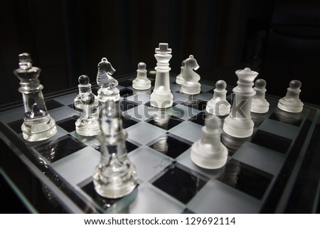 Glass chess game on a black background.The king is in the center and surrounded with different pieces.