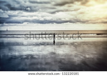 SIlhouette of a lonely person walking on a beach at low tide. Reflection of the clouds in the damp sand. This image was taken in Hendaye (Pays Basque, France).