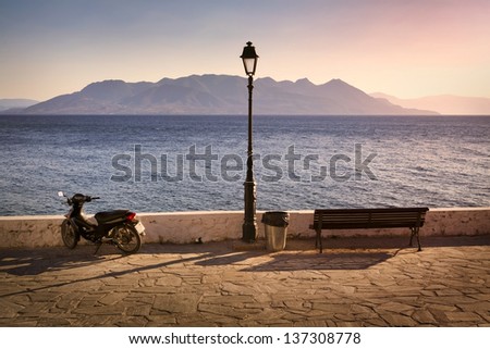 Sunset on Mediterranean Sea seen from Aegina Island with public bench and scooter in the foreground