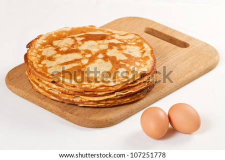 Pile of pancakes with some flour and eggs on white background