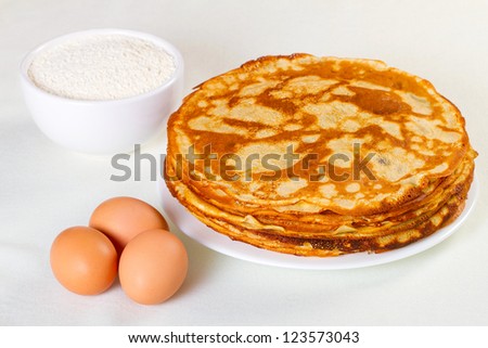 Pile of pancakes with some flour and eggs on white background