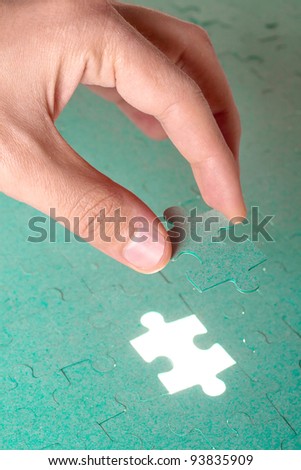 Hand inserting missing piece of green jigsaw puzzle into the hole