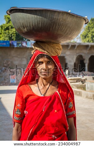 PUSHKAR, INDIA - DECEMBER 4, 2012: Unidentified Indian woman in colorful sari carries heavy basket on her head on December 4, 2012 in Pushkar, Rajasthan, India.