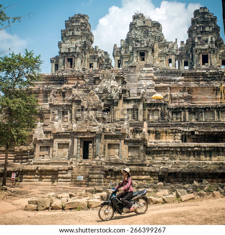 Angkor Wat, Cambodia - March 13, 2014: Unidentificate woman riding motorbike in front of old temple at Angkor wat complex