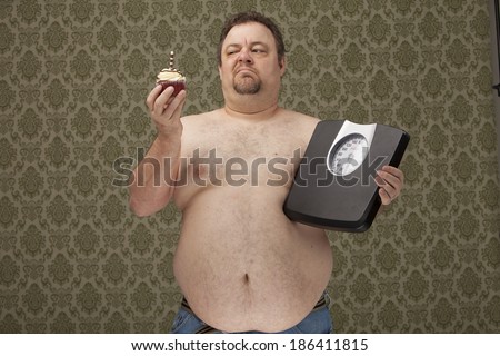 horizontal color image of an overweight male holding scales in one hand and wanting to eat the cupcake that is in his other hand