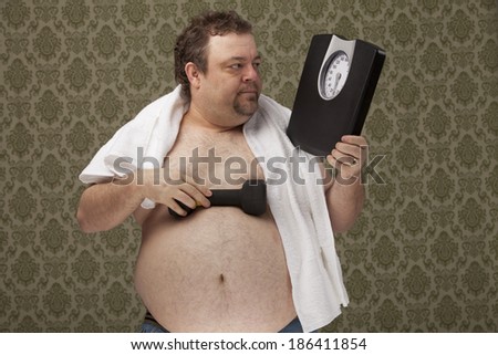 horizontal, color image of an overweight male with a towel around his neck, holding scales in one hand and weights in the other