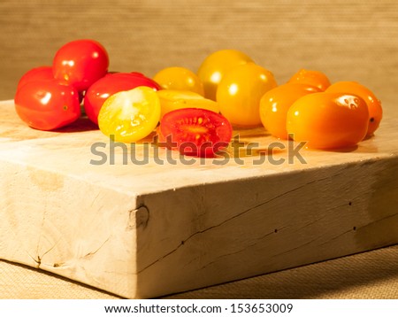 sliced red  and yellow tomatoes  on wooden chopping board with red, orange and yellow tomatoes behind