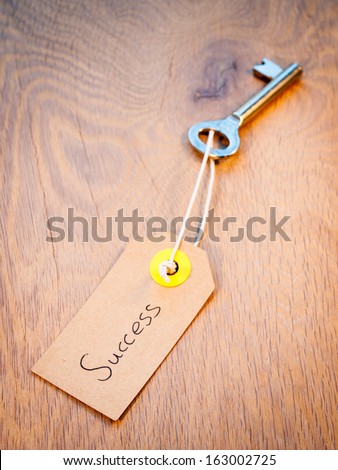 old key on a string with brown paper luggage label reading success resting on a heavily grained old wood background. Secret to successful life  concept.