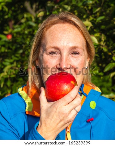 middle aged woman biting into a freshly picked red apple in an orchard
