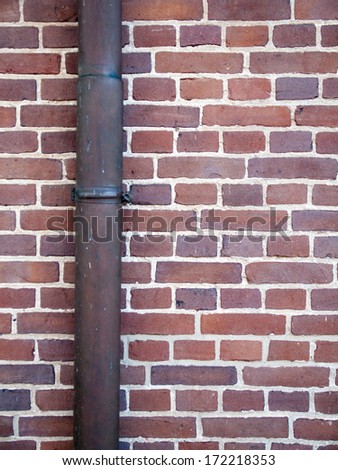 detail of drainpipe against brick wall with red-purple bricks and white mortar