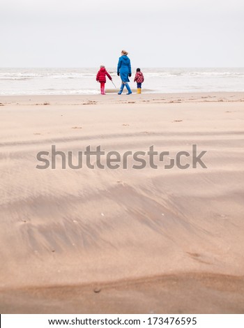 woman with small boy and girl in winter clothing and rubber boots on a winter beach looking out to sea