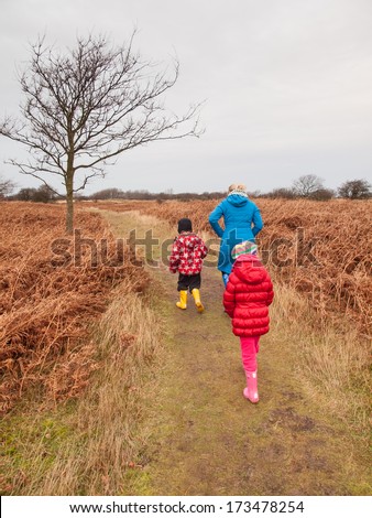 woman with small boy and girl in winter clothing and rubber boots on a winter day walking through a dune landscape