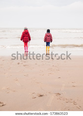 small boy and girl in winter clothing and rubber boots on a winter beach looking out to sea