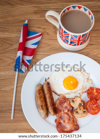 Full cooked English Break fast on a wooden table with cup of tea and British flag.