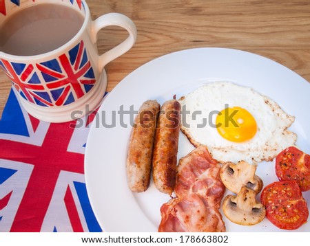 Full cooked English Break fast on a wooden table with cup of tea  and british flag.