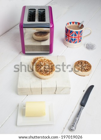 English crumpets with butter on a rustic white table top with a toaster and a cup of english tea in a union jack mug