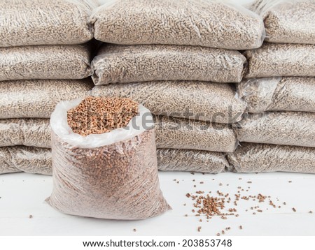An open bag of wood pellets with a stack of bagged wood pellets in storage behind