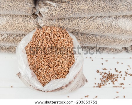 closeup of contents of an open bag of wood pellets with a stack of bagged wood pellets behind