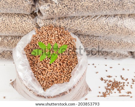 closeup of a  tree  sapling in an open bag of wood pellets with a stack of bagged wood pellets behind. Green fuel concept.