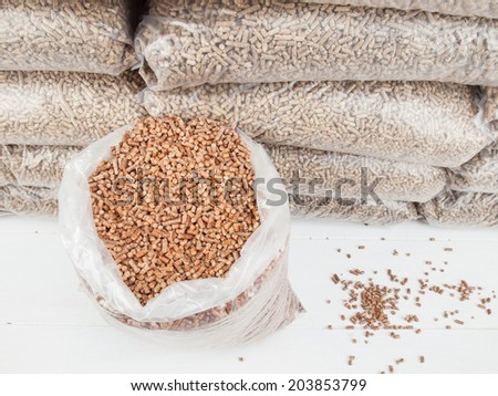 Contents of an open bag of wood pellets with a stack of bagged wood pellets behind