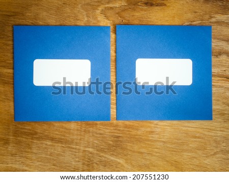 two plain blue square envelopes with blank window side by side against an aged grained wooden background