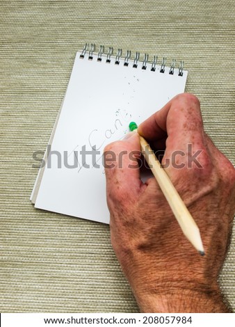 mans hand erasing the letter T from the word can\'t written in pencil on a spiral bound note pad using a pencil top eraser. positive attitude concept.