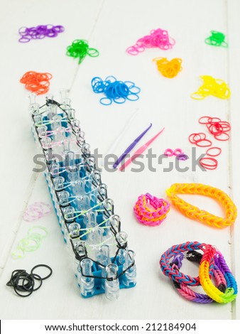 colorful elastic loom bands with band loom , bracelets, tools and hobby box against a white table top