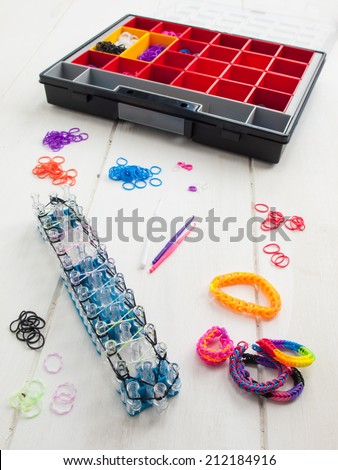colorful elastic loom bands with band loom , bracelets, tools and hobby box against a white table top