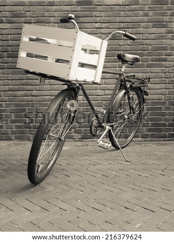 traditional delivery bike with crate viewed head on against a brick wall. toned black a white.