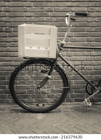 detail of traditional delivery bike with crate against a brick wall. toned black a white.