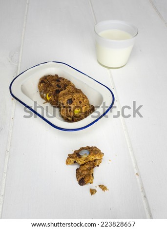 rustic home baked cookie with more cookies in an old enamel  dish and a glass of milk behind
