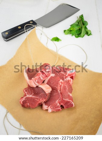 raw lamb chops on brown paper with parcel string  and fresh mint leaves and meat cleaver behind