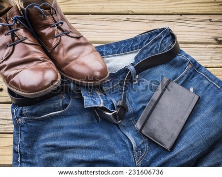 detail of blue jeans with black leather belt  against aged grainy wooden boards with notebook and brown leather shoes