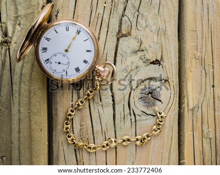 antique golden pocket watch with fob chain against rustic aged wooden background with hands approaching twelve o\'clock