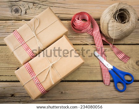 three parcels wrapped with brown paper and string with ball of string red check ribbon and scissors against an aged wooden background