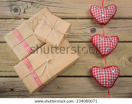 three parcels wrapped with brown paper and string with red check ribbon against an aged wooden background with red checked hearts