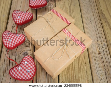 two parcels wrapped with brown paper and string with red check ribbon against an aged wooden background with red checked hearts