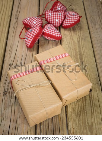 two parcels wrapped with brown paper and string with red check ribbon and red checked hearts against an aged wooden background
