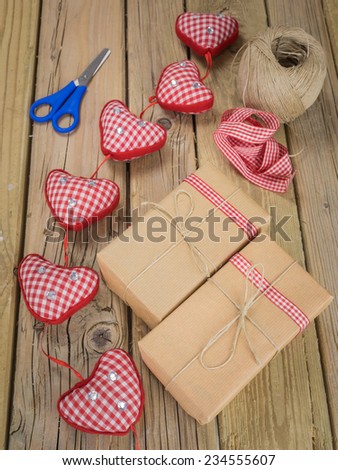 parcels wrapped with brown paper and string with ball of string red check ribbon and scissors against an aged wooden background