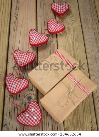 two parcels wrapped with brown paper and string with red check ribbon and red checked hearts against an aged wooden background
