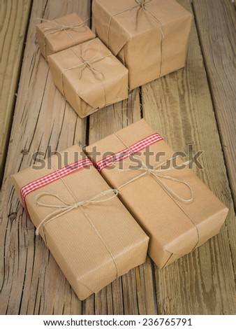 string and brown paper parcels on a grainy cracked aged wooden table decorated with red checked ribbon