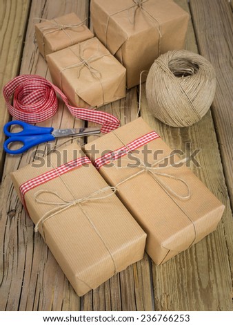 string and brown paper parcels on a grainy cracked aged wooden table with ball of string and red checked ribbon and scissors