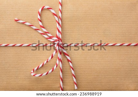 detail of string and brown paper parcel:red and white striped  string bow against brown wrapping paper