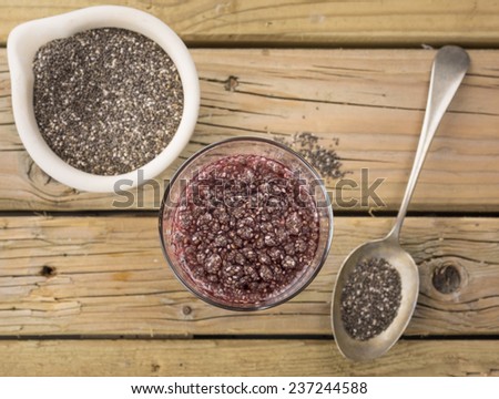 overhead view of chia seed drink with a spoon and bowl of black and white chia against aged knotted wooden background in soft focus behind